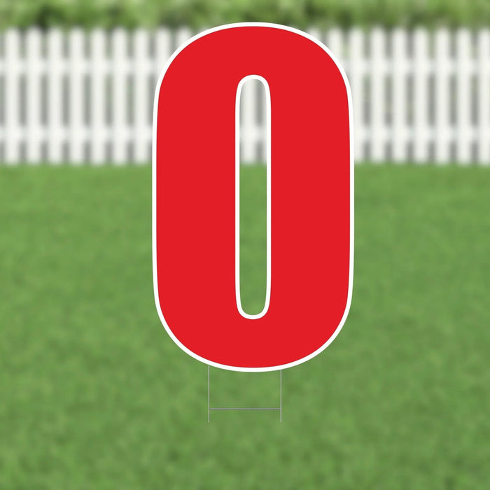 Red letter O yard sign with white border and metal stakes, displayed on a lawn with white picket fence in background.