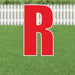 Large red letter R yard sign with white outline and metal stakes, displayed on green grass with white picket fence background.