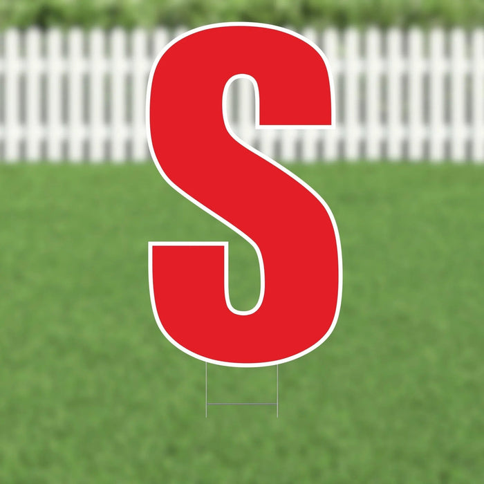 Large red letter S yard sign with white outline and metal stakes, displayed on green grass with white picket fence background.
