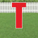 Red letter T yard sign with white border and metal stakes, displayed on green grass with white picket fence background.