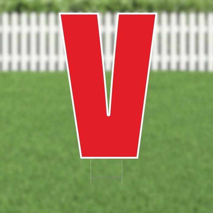 Red letter V yard sign with white border and metal stakes displayed on green grass with white picket fence in background.