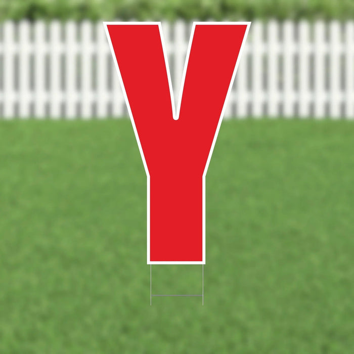 Red letter Y yard sign with white border and metal stake, displayed on green grass with white picket fence background.