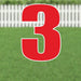 Large red number 3 yard sign with white outline and metal stakes, displayed on green grass with white picket fence in background.