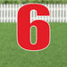 Large red number 6 yard sign with white outline and supporting stakes, displayed on green grass with white picket fence background.