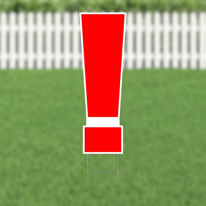 Red exclamation point yard sign with white border and metal stakes, displayed on grass with white picket fence in background.