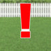 Red exclamation point yard sign with white border and metal stakes, displayed on grass with white picket fence in background.