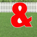 Large red ampersand symbol with white outline and cutout details, displayed in a yard against a white picket fence.